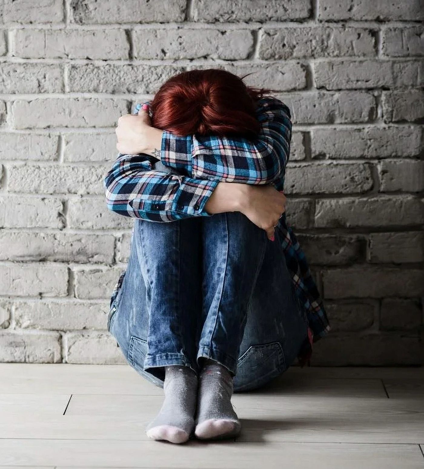 Young woman sitting against a wall, looking down