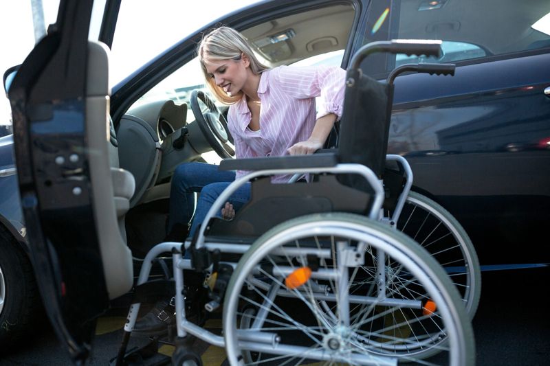Carer helping a woman from her wheelchair into a car