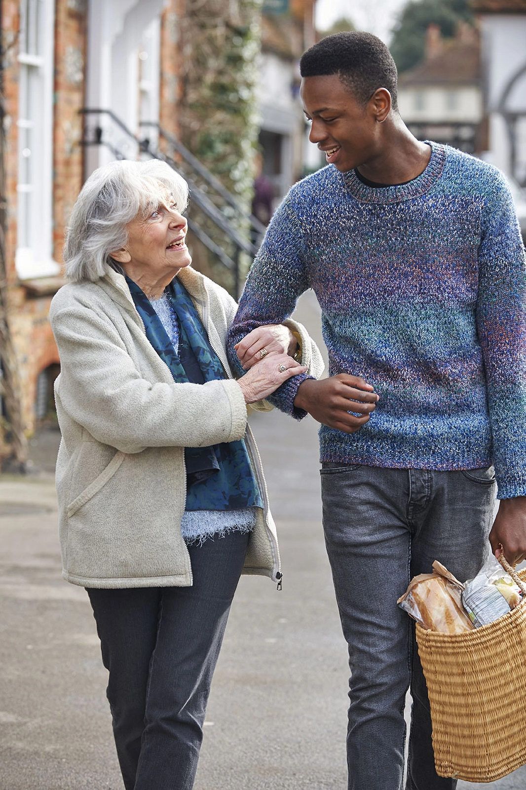 A young carer walking arm in arm with a smiling older woman outside her home